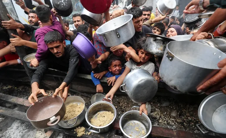 Palestinians wait to receive food cooked by a charity kitchen